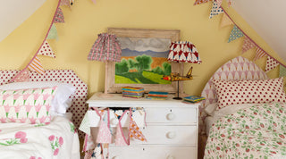 An attic room with twin single beds upholstered headboards, cushions, eiderdowns and lampshades to match in molly mahon's hand block printed greencombe collection bringing uplifting colour and joy to the space