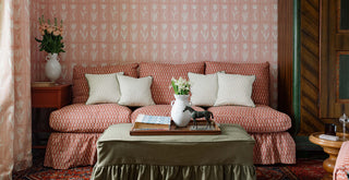 Terracotta patterned sofa against pink floral wallpaper with decorative pillows in english cottage styling.