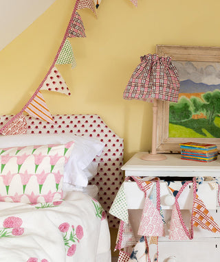 Attic room spilling over with Molly Mahon's hand block printed designs on headboards, quilts, cushions, lampshades, and bunting with two single beds separated by a small chest of draws