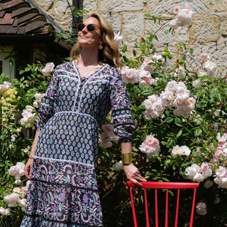 Molly Mahon in a patterned dress standing in front of a stone wall and flowers