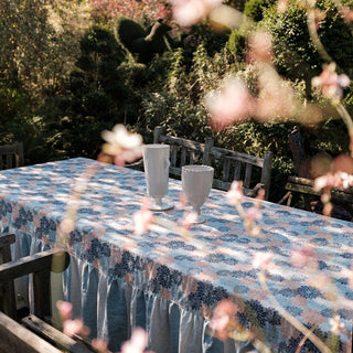 Outdoor table setting with floral tablecloth and glasses, surrounded by greenery.