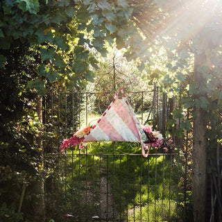 Striped fabric with floral elements hanging on a metal gate surrounded by greenery.