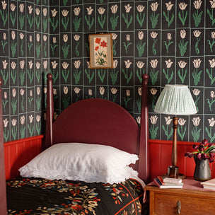 Bedroom with  black green floral wallpaper, red headboard, and wooden nightstand.