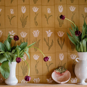 Two vases with tulips against Molly Mahon Botanica wallpaper in gold olive.