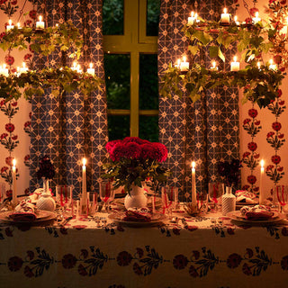 Image of a table laid out for Christmas dinner, molly mahons new dianthus wallpaper in indigo and iron lining the wall, her new table cloth in the same colour spread on the table and her new dianthus napkins, again in the same colour laid on the plates. A vase of red flowers in the centre of the table and 4 candles lit.