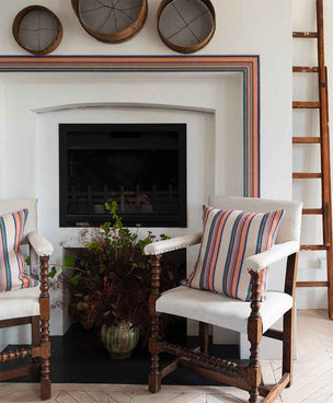 Image of Molly Mahon cushions made from the Odisha fabric with the cream base placed on chairs in front of a fireplace which is framed by Molly Mahons Odisha trim.