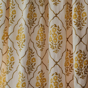 A close-up of a curtain or fabric panel with a repeating floral trellis pattern in mustard yellow and olive green on a warm off-white background.