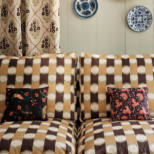 A sofa upholstered in a brown, beige, and cream ikat-style patterned fabric, styled with two decorative throw pillows in a living room setting.