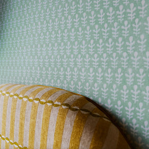 A close-up of a striped bed head in front of turquoise green wallpaper with a repeating leaf pattern.
