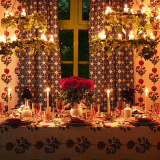 Image of a table laid out for Christmas dinner, molly mahons new dianthus wallpaper in indigo and iron lining the wall, her new table cloth in the same colour spread on the table and her new dianthus napkins, again in the same colour laid on the plates. A vase of red flowers in the centre of the table and 4 candles lit.