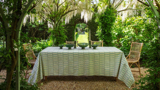 Dining table set outdoors with a green and white striped luna tablecloth in a garden setting.