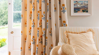 Kitchen curtains made in Molly Mahon's Poppy hand block printed fabric design with an armchair in yellow stripes and a cushion designed by Molly in her Seed mustard design