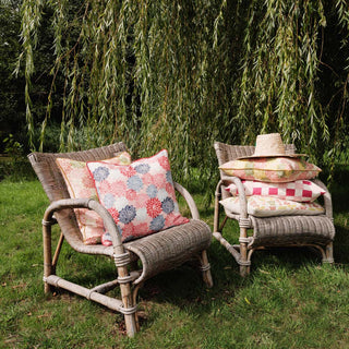 Two wicker chairs with colorful cushions in a garden setting with willow trees.