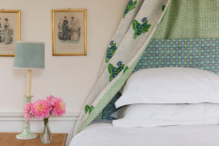 floral fabric by molly mahon hand block printed primrose in greens and blues backed by the design seed in green as a valance over an headboard upholstered in a trellis design in matching colours on a double bed