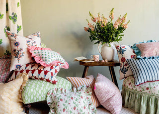 Cushions piled up in front of Molly Mahon Dianthus hand blocked fabric with an arm chair upholstered in Strawberry design