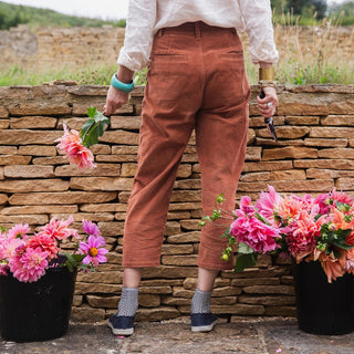 Molly Mahon in brown pants standing next to potted flowers against a stone wall.