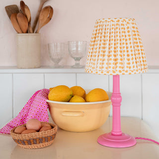 molly mahon's seed hand block printed design pleated lampshade in yellow sitting on top of the twig pink lamp base bring bright bold colours in the kitchen sitting nicely against a bowl of lemons