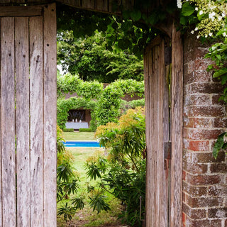 Garden view of table setting through a wooden archway with a pool and greenery.